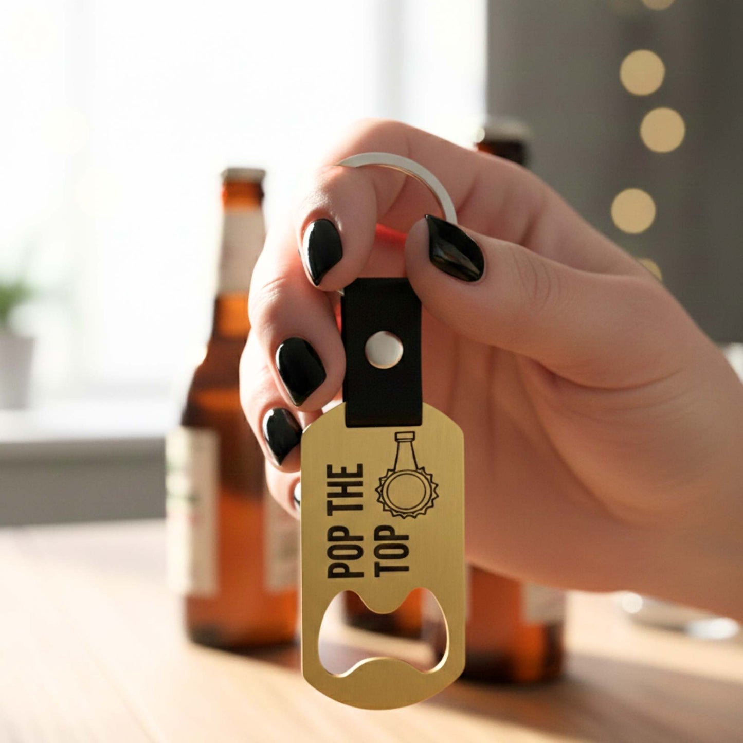 Llavero personalizado tipo abrebotellas en acero dorado con la frase "POP THE TOP", sostenido por una mano con fondo de botellas.